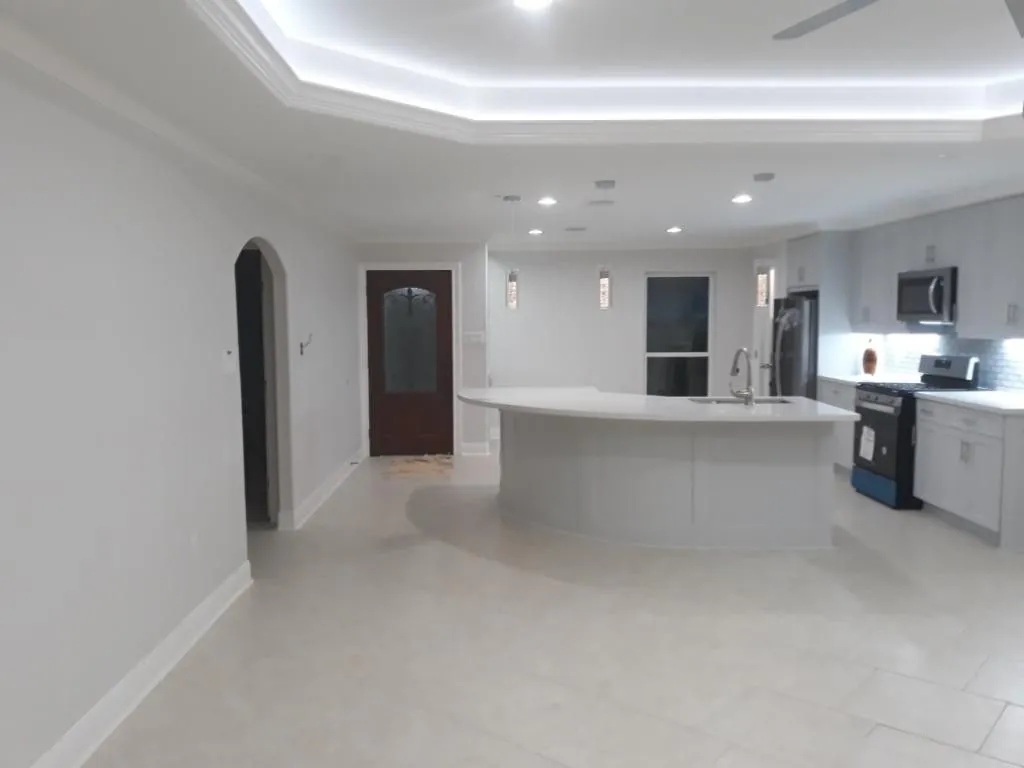 Open plan kitchen with a curved quartz island, white cabinets and a lit tray ceiling